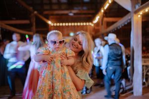 People share a joyful dance moment at a rustic venue decorated with warm string lights during an evening celebration.