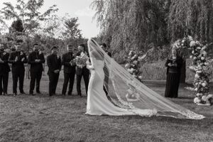 Black and white wedding ceremony photo showing long flowing veil and attendants in formal attire.