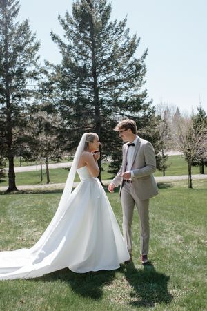 A wedding couple stands together on a sunny spring day with tall pine trees in the background.