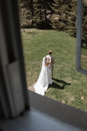 A bride in a flowing white wedding dress walks across a sunny grassy hillside on a spring day.