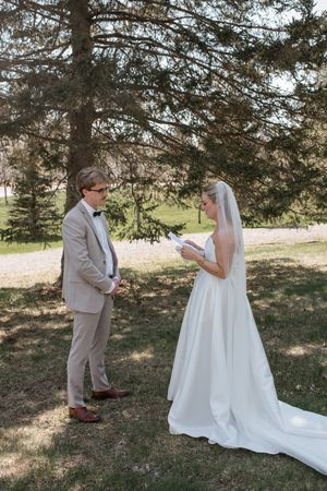 A couple shares a touching first look moment in an outdoor setting under pine trees during their wedding ceremony.