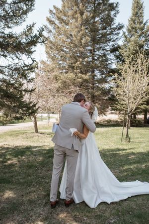 A tender embrace between newlyweds surrounded by pine trees in natural outdoor setting.