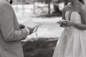 Black and white photo capturing intimate vow reading moment during outdoor wedding ceremony.