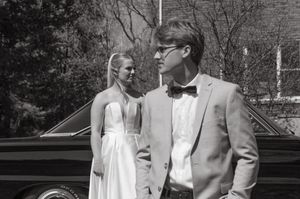Classic black and white wedding portrait beside a vintage car during an outdoor photoshoot.