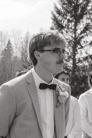 Several groomsmen in light gray suits and bow ties stand together at an outdoor wedding ceremony.