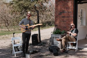 Musicians performing outdoors with acoustic guitar and percussion instruments.