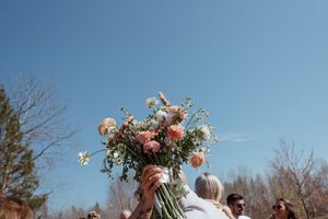 Wedding guests holding up a colorful bouquet of flowers against a bright blue sky.