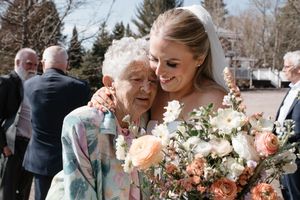 A tender moment between young and elderly wedding guests as they embrace, with soft peach roses in the bouquet.
