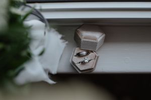An elegant engagement ring nestled in a gray velvet box on a white windowsill.