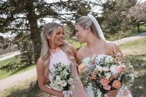 Bridesmaids in pink dresses embrace and share loving moments while holding pastel flower bouquets during outdoor photoshoot.