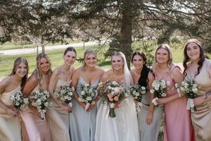 Wedding party in pastel dresses posing together outdoors with floral bouquets.