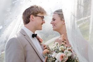 A joyful wedding couple shares an intimate moment outdoors while the bride holds a soft pink and white bouquet.