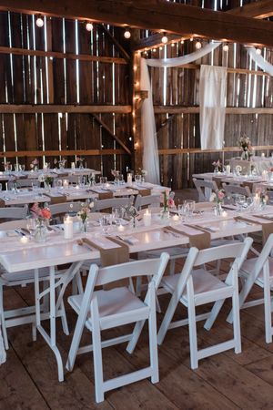 Rustic barn wedding reception setup with white chairs and elegant table settings.