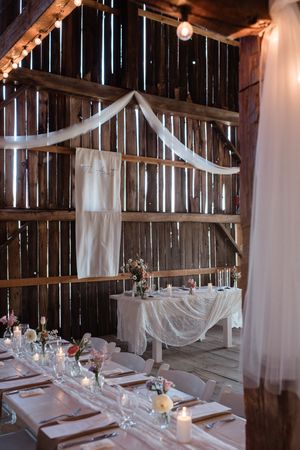 Elegant barn wedding table settings with flowing white fabric draping and string lights.