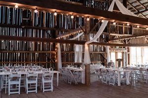 Rustic barn wedding reception venue with white folding chairs and draped fabric decorations illuminated by string lights.