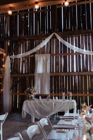 Rustic barn wedding reception setup with white draping, string lights and elegantly set dining tables.