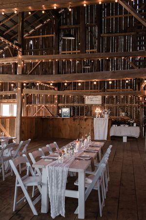 Rustic barn interior decorated with string lights and white dining tables for wedding reception.