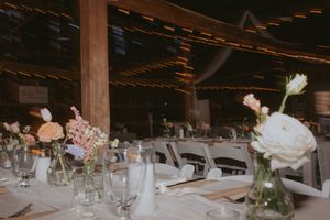 Elegant table setting with floral centerpieces in glass vases inside a rustic wooden barn reception venue.