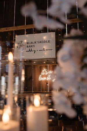 Black Saddle Barn sign illuminated with romantic lighting and hanging decorations.