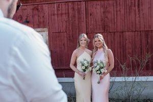 Two bridesmaids in light pink dresses stand with bouquets in front of a rustic red barn.