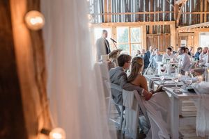 Wedding reception candid shot through curtains showing decorated barn dining space.