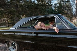 A classic black vintage car photographed with occupants leaning out the window in a playful pose.