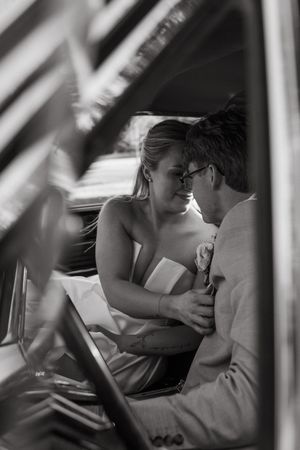 A romantic black and white photo of newlyweds sharing an intimate moment in a car after their wedding ceremony.