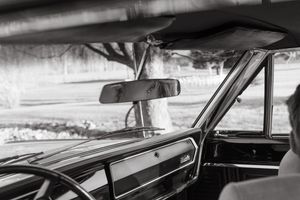 Black and white view through vintage car windshield showing rearview mirror and classic dashboard.