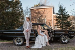 A vintage black car serves as backdrop for a wedding photo with a bride in white gown.