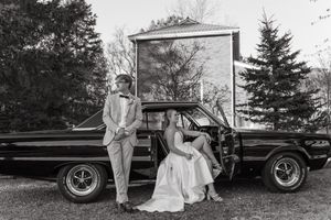 Classic black car parked outdoors during a formal wedding photo session with elegant dressed figures in the scene.