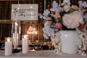 Elegant wedding decor with white candles, floral arrangements, and a Black Saddle Farm sign illuminated by warm lighting.