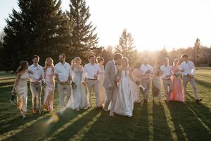 Wedding party poses together in golden sunset light with rays streaming through pine trees in natural outdoor setting.
