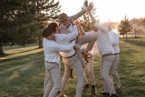 A playful moment at a wedding with groomsmen celebrating together on a sunlit lawn.