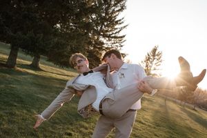 A joyful wedding moment captured in golden sunlight as the groom carries the bride.