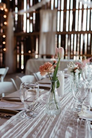 Elegant wedding table setting with crystal glasses and delicate floral centerpiece in rustic barn venue.