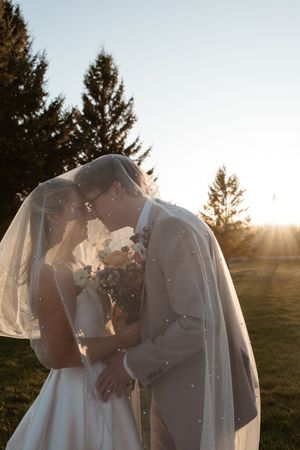 A romantic sunset wedding portrait of a couple embracing under a flowing veil.