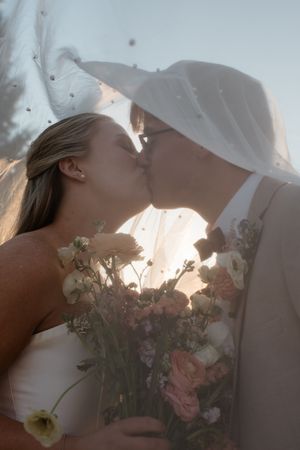 A romantic wedding moment captured with a flowing veil and delicate bouquet of pink flowers at sunset.