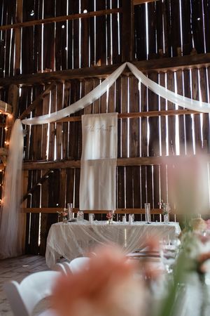 Wedding dress hanging in rustic barn setting with draped fabric and string lights.