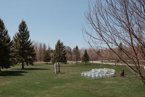 Outdoor wedding ceremony setup with white chairs on green lawn surrounded by evergreen trees.