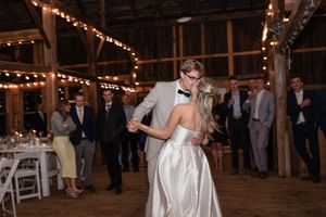 A couple shares their first dance in a rustic barn venue decorated with twinkling string lights.