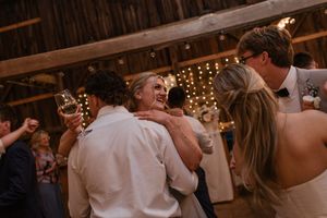 Wedding guests dancing and celebrating in a barn venue with twinkle lights overhead.