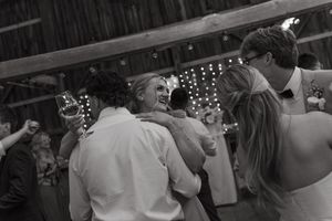 Black and white photo of joyful dancing at a wedding reception with twinkling lights in the background.
