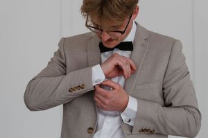 Close-up shot of someone adjusting a cufflink while wearing a light gray suit and black bowtie.