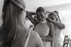 People helping with wedding dress preparations in a bright sunlit room.