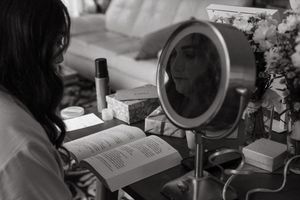 Black and white photo of preparation setup with makeup mirror, book and beauty supplies.