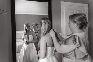Wedding preparations being made by individuals in formal attire looking at a reflection in a mirror.