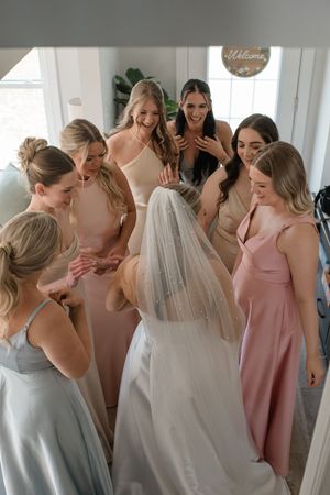 A bridal party shares a joyful moment together, wearing pastel bridesmaid dresses in pink, peach and grey tones.