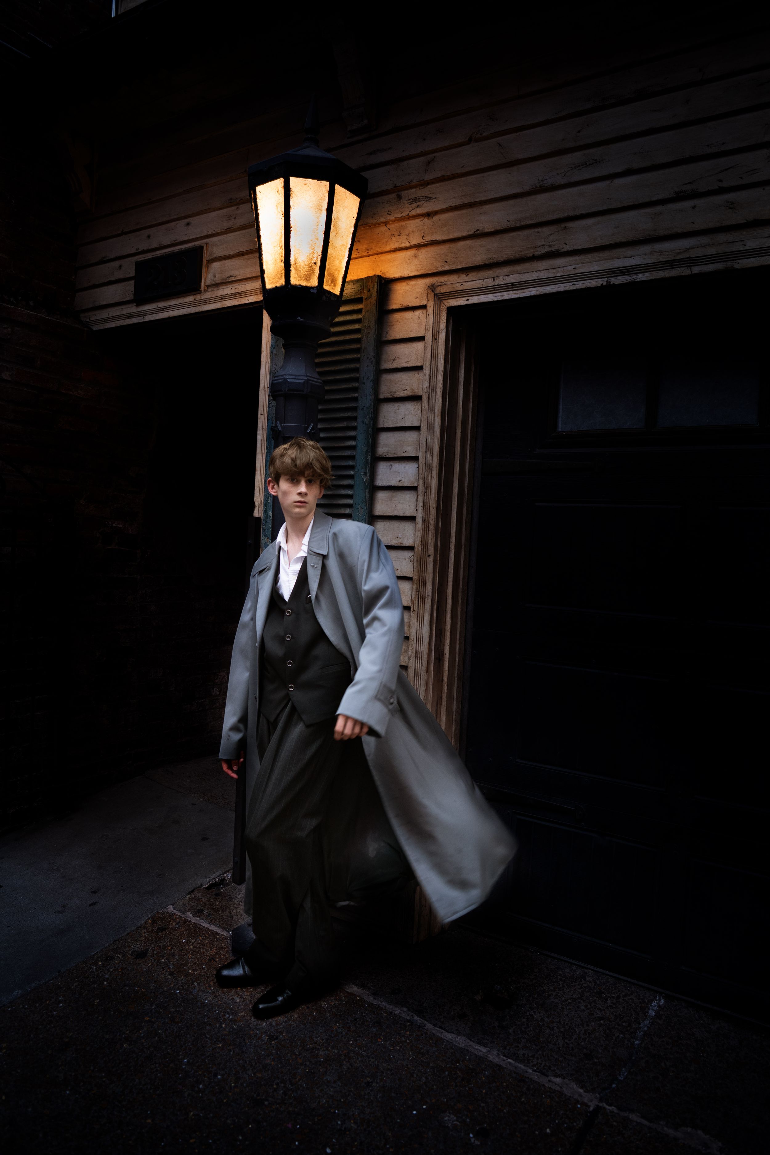 A dark moody series of photos showing a figure in a suit and coat standing near an illuminated porch light.