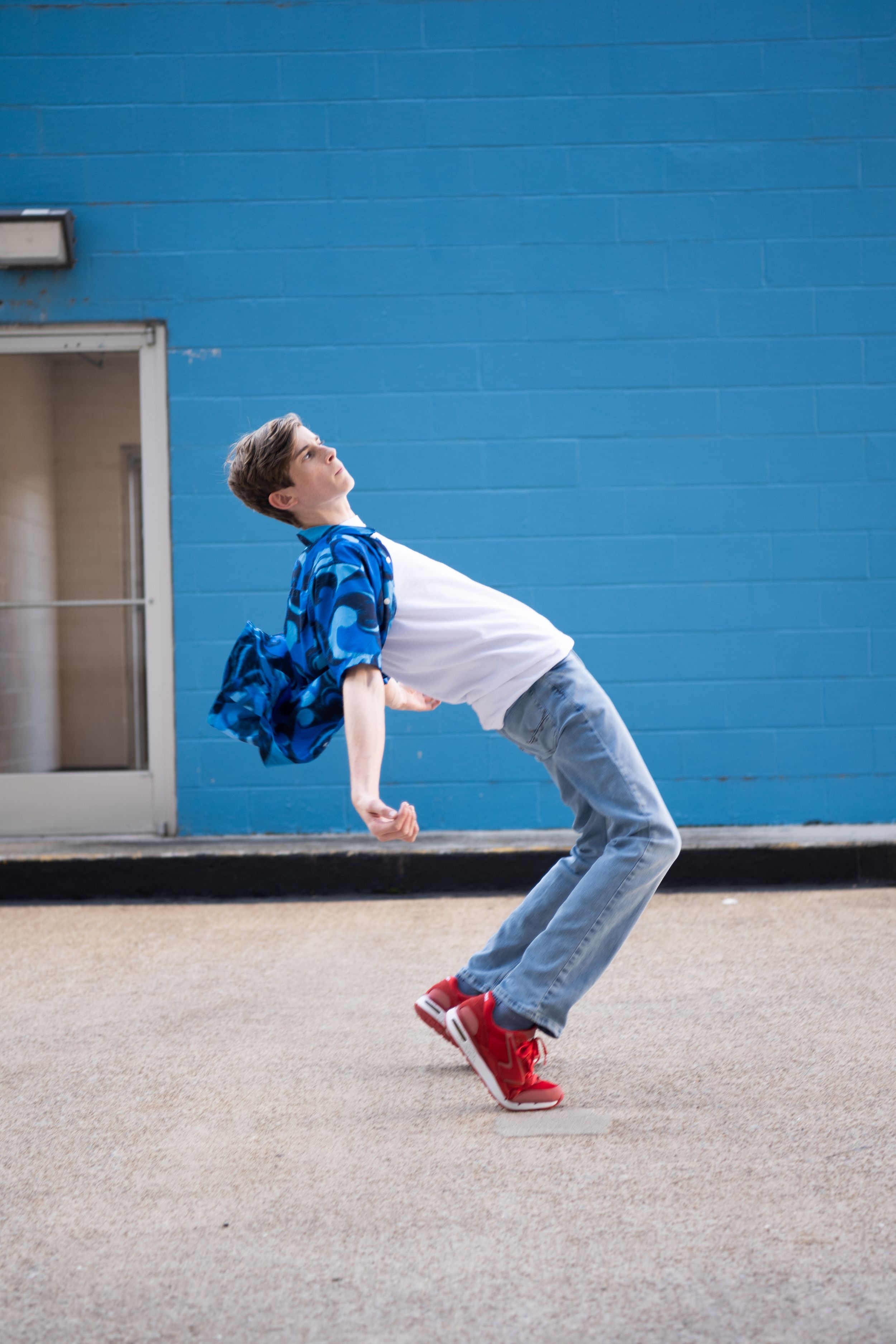 A sequence of photos showing a person in jeans and red shoes falling backwards against a bright blue wall.