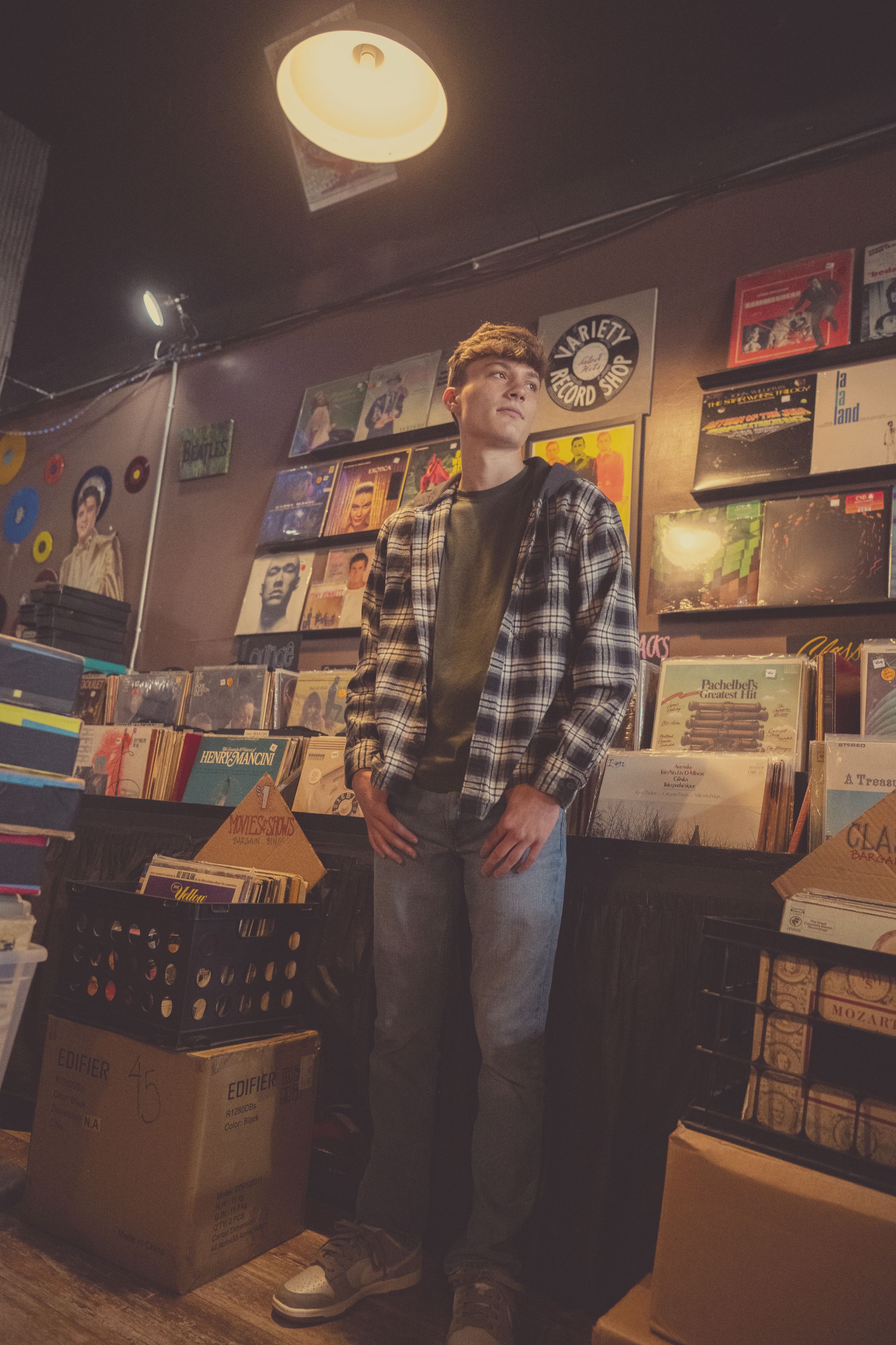 A dimly lit record store interior with vinyl albums displayed on shelves and walls creating a cozy atmosphere.